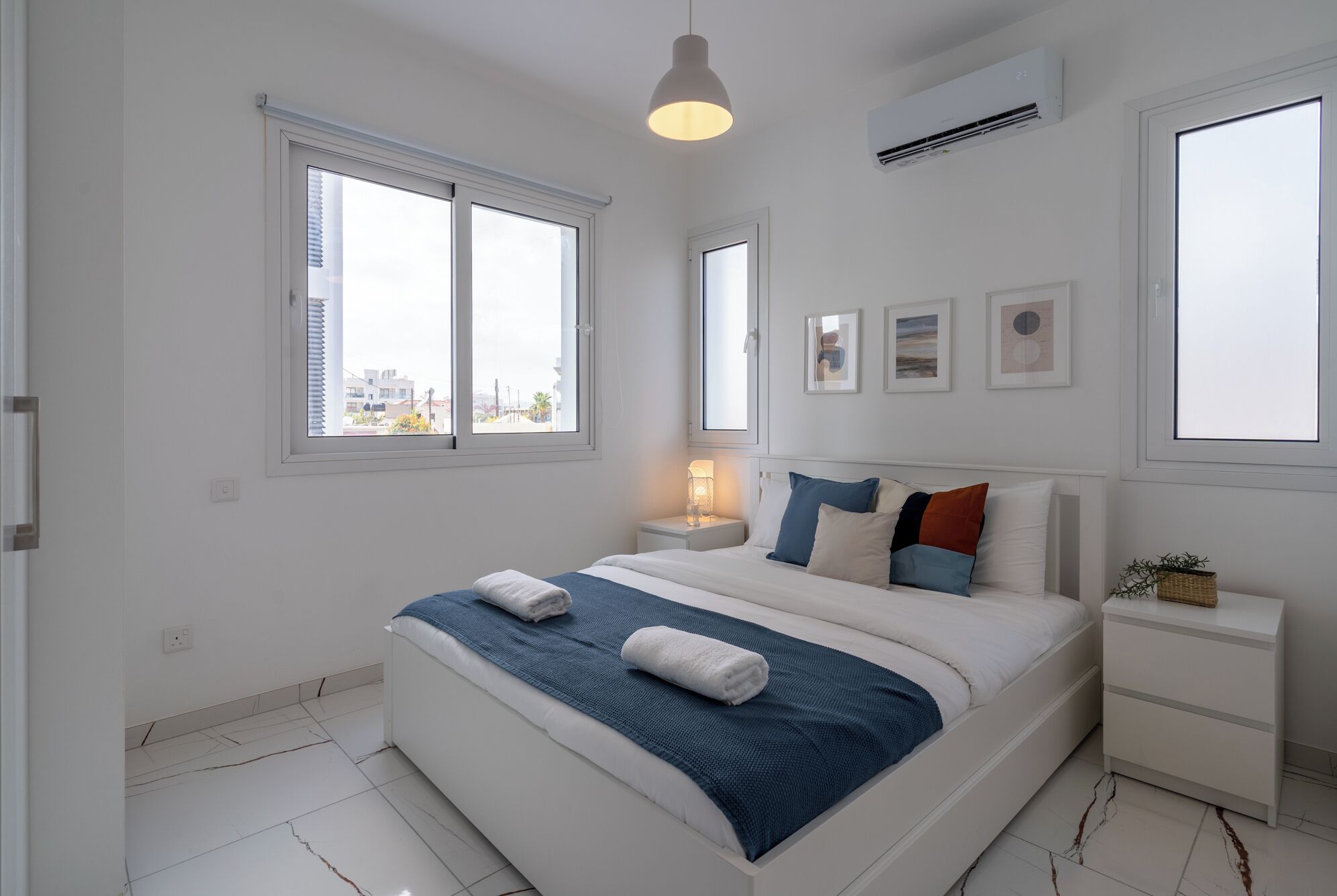 A modern bedroom with a large bed, a bedside table, a nightstand, and a window with a city view.