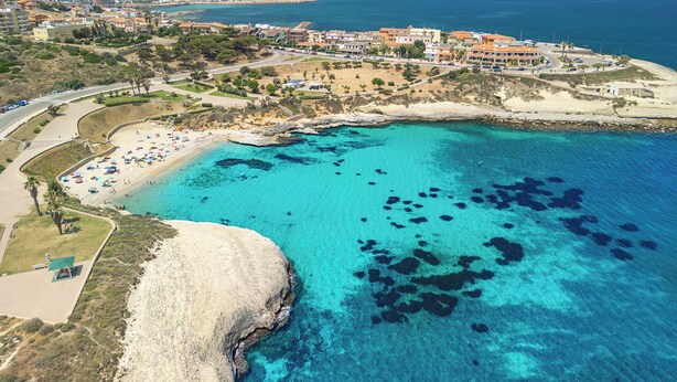 Vue aérienne d’une zone côtière avec une plage, des eaux d’un bleu limpide et un port de plaisance.