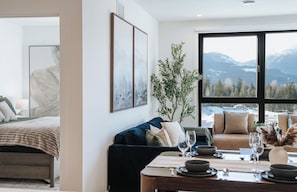 Una sala de estar moderna con comedor, un ventanal con vistas a la montaña y una zona de estar acogedora.