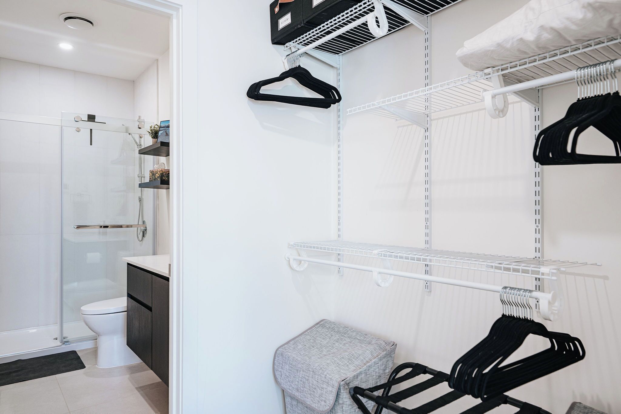 A modern bathroom with a glass shower enclosure, a white toilet, and a built-in shelf with a towel rack.