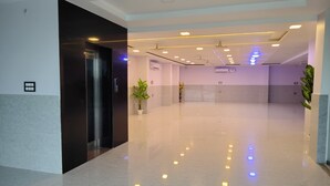 A spacious, well-lit hallway with a modern design, featuring a black elevator, potted plants, and recessed ceiling lighting. - Hotel Shree Park Ayodhya (Faizabad)