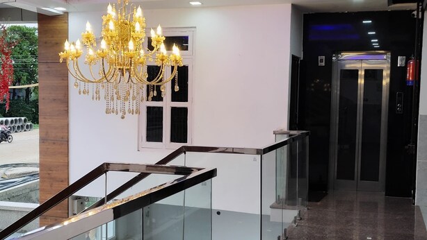 A modern lobby with a glass staircase, a chandelier, and an elevator. - Hotel Shree Park Ayodhya (Faizabad)