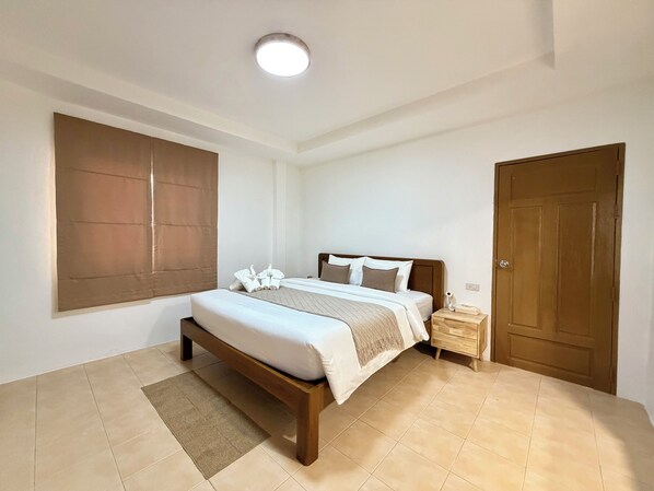 Ein Schlafzimmer mit Bett, Nachttisch, Tür und einem Fenster mit Jalousien.