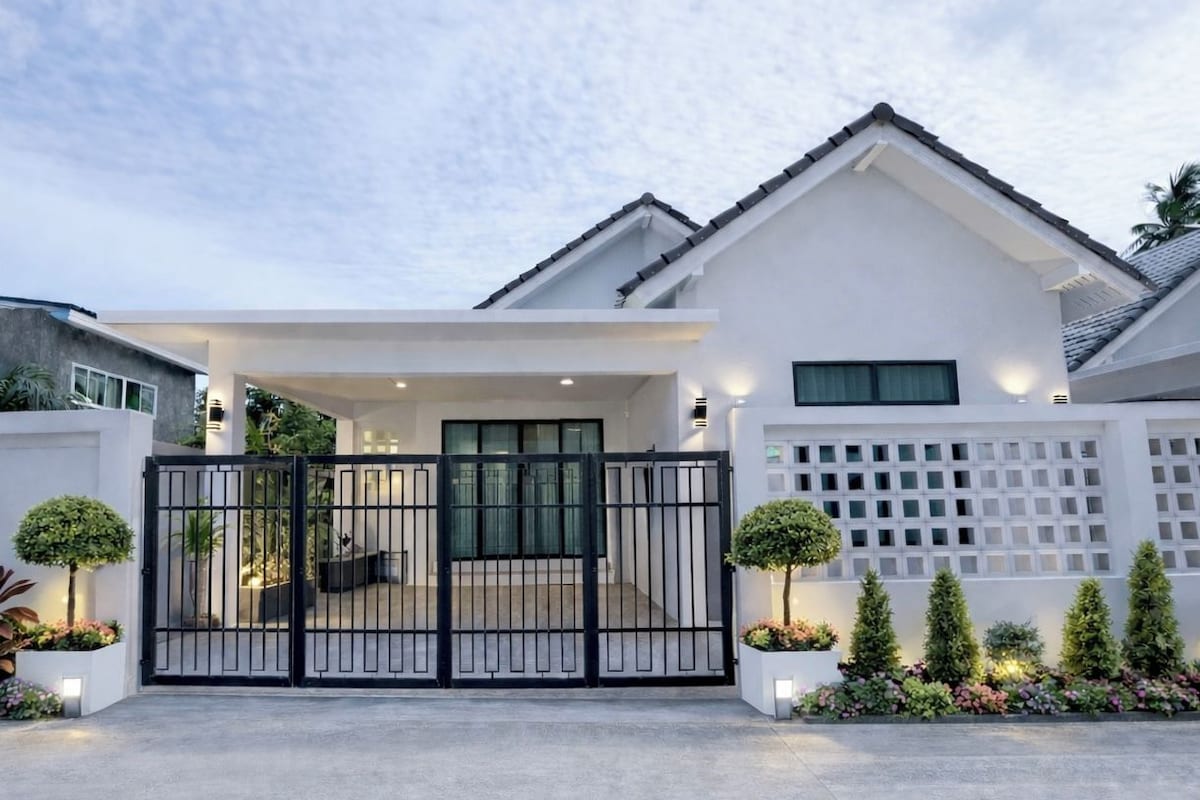 Een modern huis met een hek, een overdekte veranda en een witte schutting met een lattenstructuur.