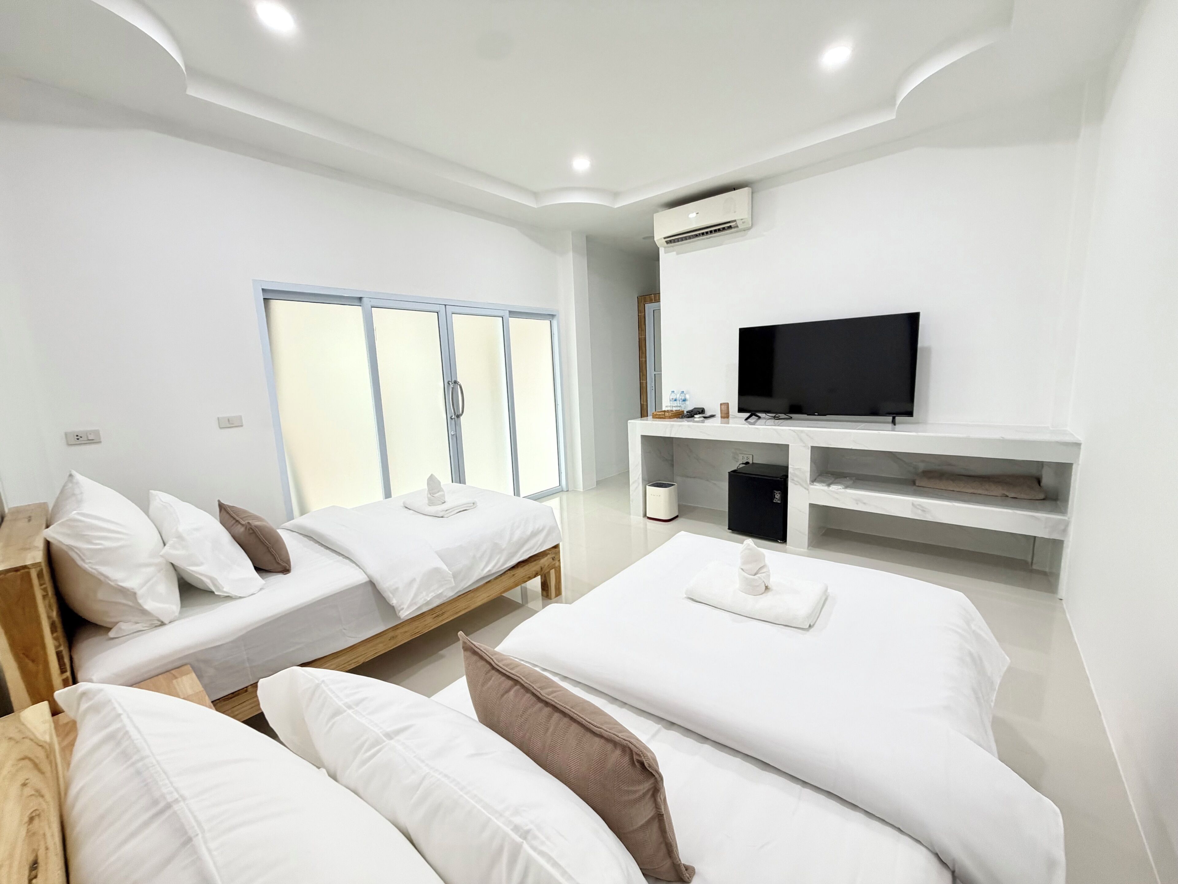A hotel room with two beds, a TV, a minibar, and a large window.