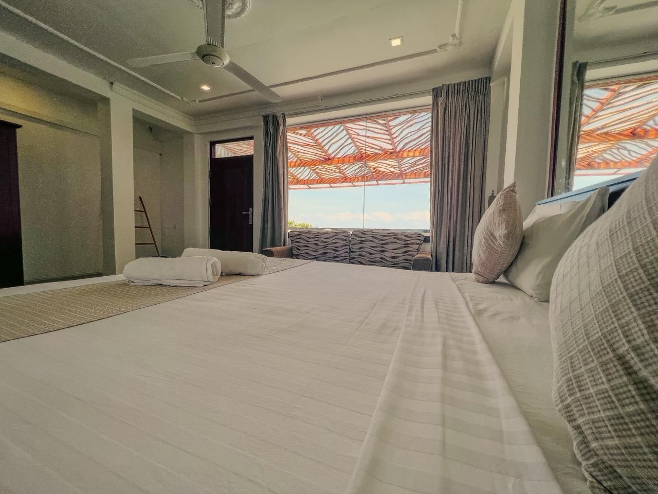 A hotel room with a large bed, a view of the outdoors, and a ceiling fan.