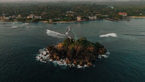 An aerial view of a coastal area with a rocky island surrounded by clear blue waters. - Beach House Goviyapana (Matara Road, Goiyapana,)