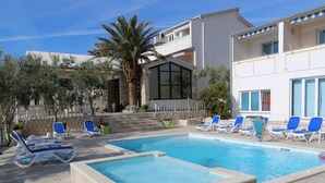 A swimming pool with lounge chairs, a palm tree, and a stone wall. - Seaside 3-bedroom Luxury Penthouse (Novalja)