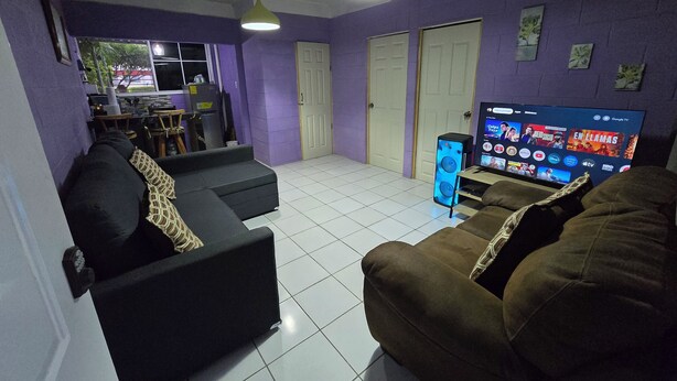 A living room with a black sofa, a brown sofa, a TV, and a speaker. - Centrally located and private apartment with its own home theater with giant screen (Santa Ana)
