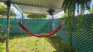 A hammock under a metal roof, surrounded by a green fence and grass. - Centrally located and private apartment with its own home theater with giant screen (Santa Ana)