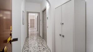 Un couloir avec une porte blanche, une armoire blanche et un sol carrelé.