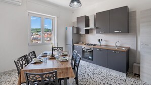 Une cuisine moderne avec des meubles gris, une table à manger en bois et une vue sur les bâtiments environnants.