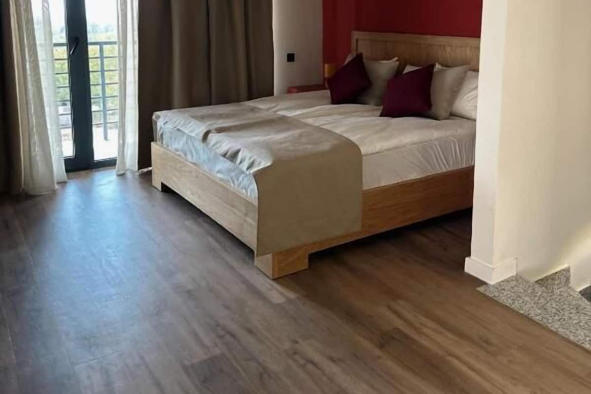 Une chambre avec un lit en bois, un mur d’accent de couleur rouge et une grande fenêtre avec des rideaux.