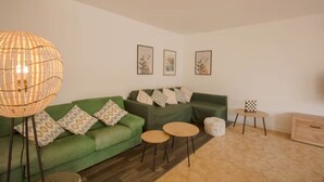 Una sala de estar moderna con un sofá verde, dos mesas redondas, una lámpara de pie y cuadros enmarcados en la pared.