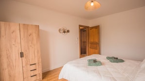 Un dormitorio con un armario de madera, una cama con ropa de cama blanca y una lámpara colgante.
