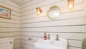 A bathroom with a white toilet, a pedestal sink, and two wall-mounted light fixtures. - Shades Farm Summerhouse (Swindon)