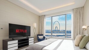 A hotel room with a large TV displaying "NETFLIX," a bed with pillows, a chair, and a view of a Ferris wheel. - LUX Iconic Views at Palm Tower Suite 7 (Dubai)