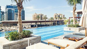 A rooftop pool area with lounge chairs and palm trees, overlooking a cityscape with high-rise buildings. - LUX Iconic Views at Palm Tower Suite 7 (Dubai)