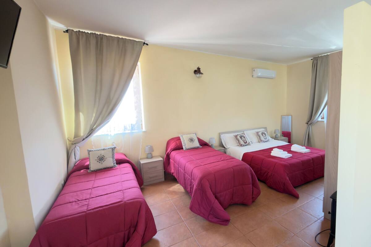 A hotel room with two beds, a nightstand, a lamp, and a window with curtains.