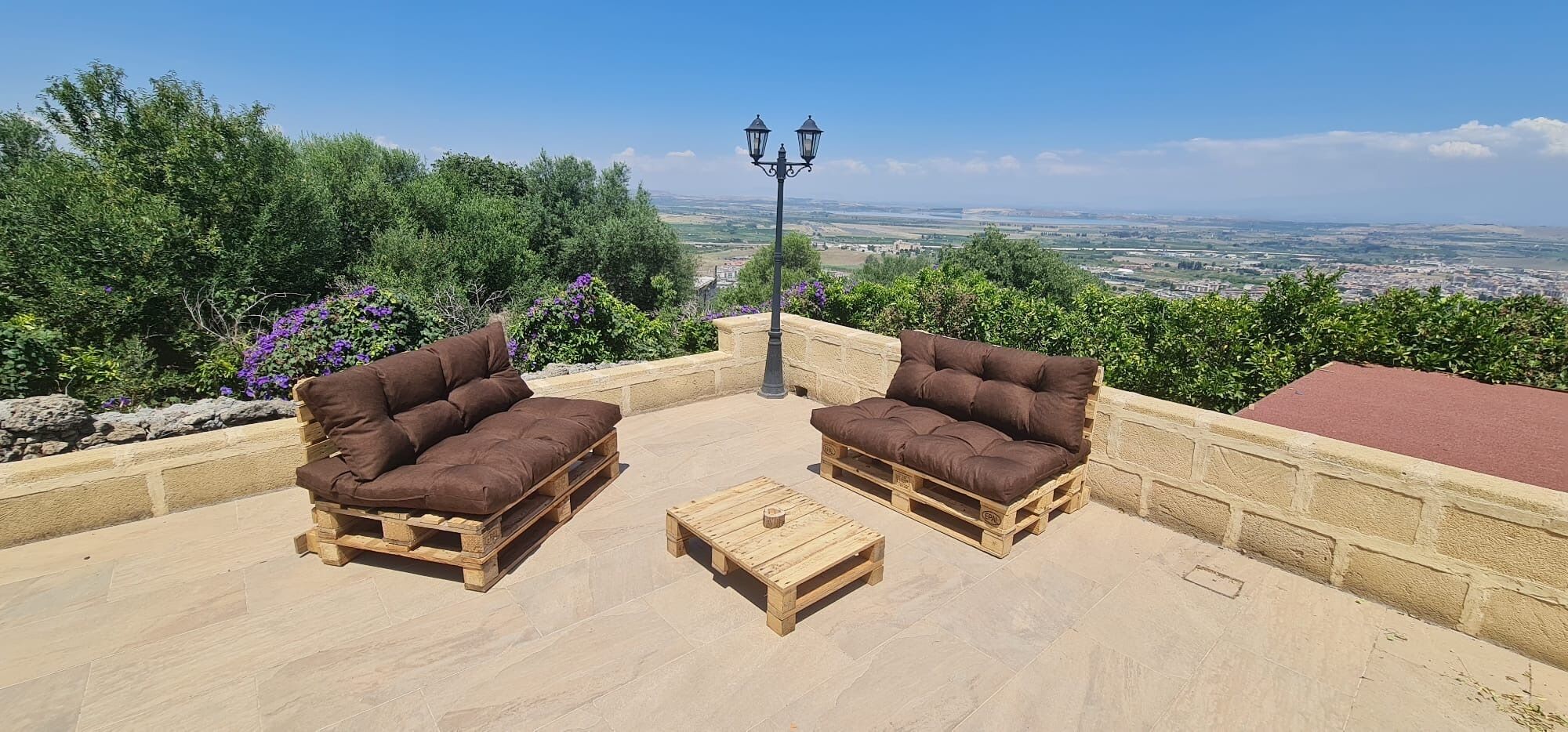 Une terrasse avec deux canapés en bois, une petite table en bois et un lampadaire.