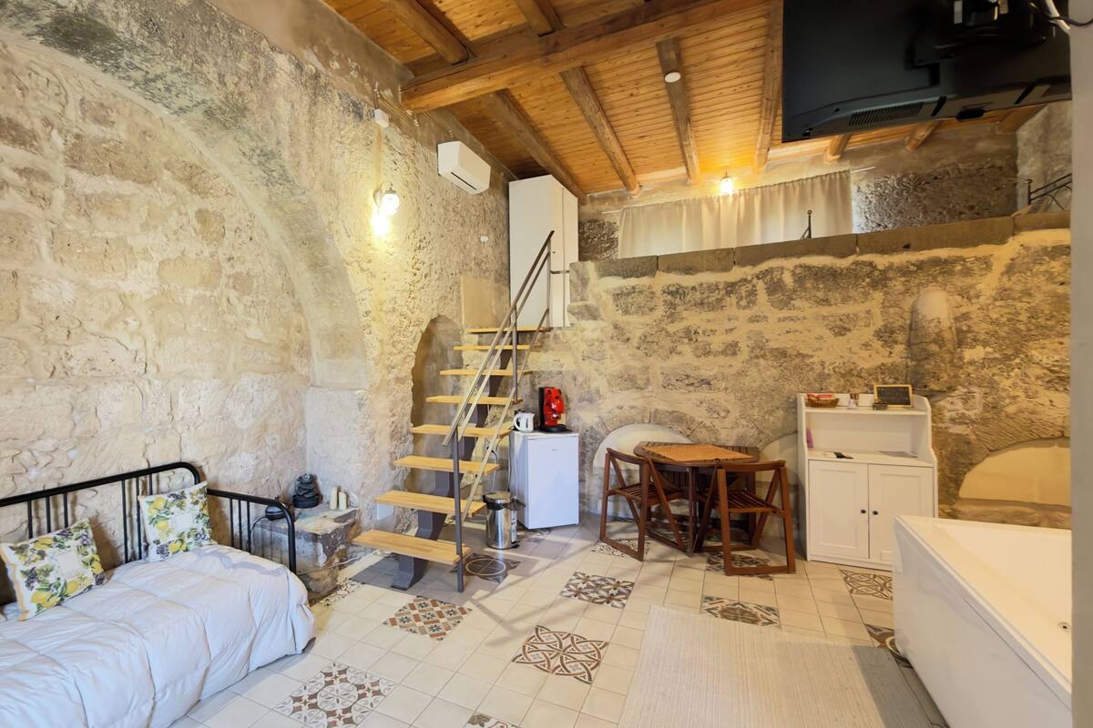 A rustic room with a bed, a wooden ladder, a small table, and a white cabinet.