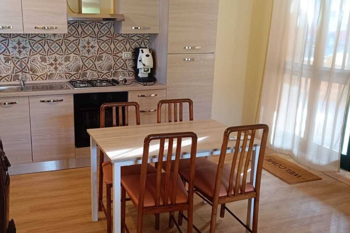 A compact kitchen with a dining area, featuring a tiled backsplash, a coffee machine, and a stove.