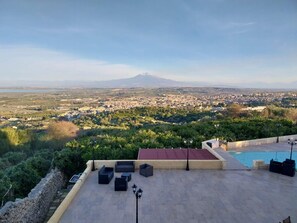 Terraza en la azotea con mobiliario exterior, piscina y vistas a un paisaje urbano y a la montaña.
