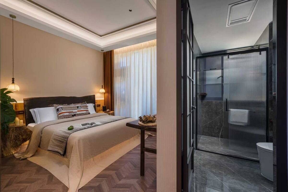 Une chambre d’hôtel avec un grand lit, une table de chevet et une vue sur une salle de bain moderne dotée d’une douche à parois de verre.