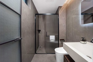 A modern bathroom with a glass shower enclosure, a white toilet, and a white sink with a mirror above it.
