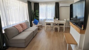 A living room with a sofa, dining table, chairs, a ceiling fan, and a TV. - 3-bedroom peaceful house with backyard, EV charger (and free parking), and AC (Macquarie)