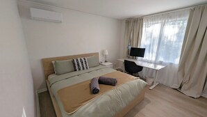 A hotel room with a bed, a desk, a computer, and a window with curtains. - 3-bedroom peaceful house with backyard, EV charger (and free parking), and AC (Macquarie)