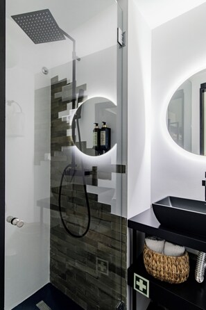 A modern bathroom with a glass-enclosed shower, a round mirror, and a black vanity with a woven basket. - Regras Apartments & Garden B12 by Benefit Collection (Porto)