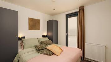 Une chambre à coucher avec un lit, des lampes de chevet, un radiateur et une fenêtre avec des rideaux.