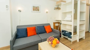 Een moderne woonkamer met een grijze bank, oranje kussens, een houten tafel met een fruitschaal, en een wit kastenmeubel.