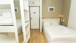 Ein Hotelzimmer mit einem Etagenbett, einem Einzelbett, einer Tür und einer an der Wand montierten Lampe.