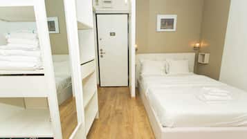 A hotel room with a bunk bed, a single bed, a door, and a wall-mounted light fixture.
