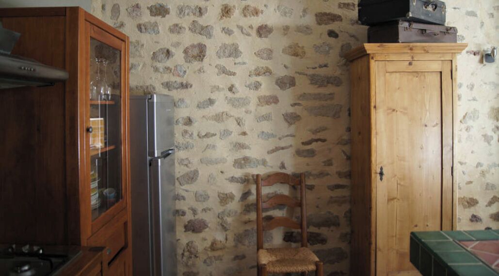 A kitchen with a refrigerator, wooden cabinets, and a stone-patterned wall.