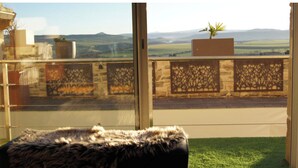 Un balcon donnant sur des collines ondoyantes, une plante en pot et un mur de pierre orné de motifs complexes.