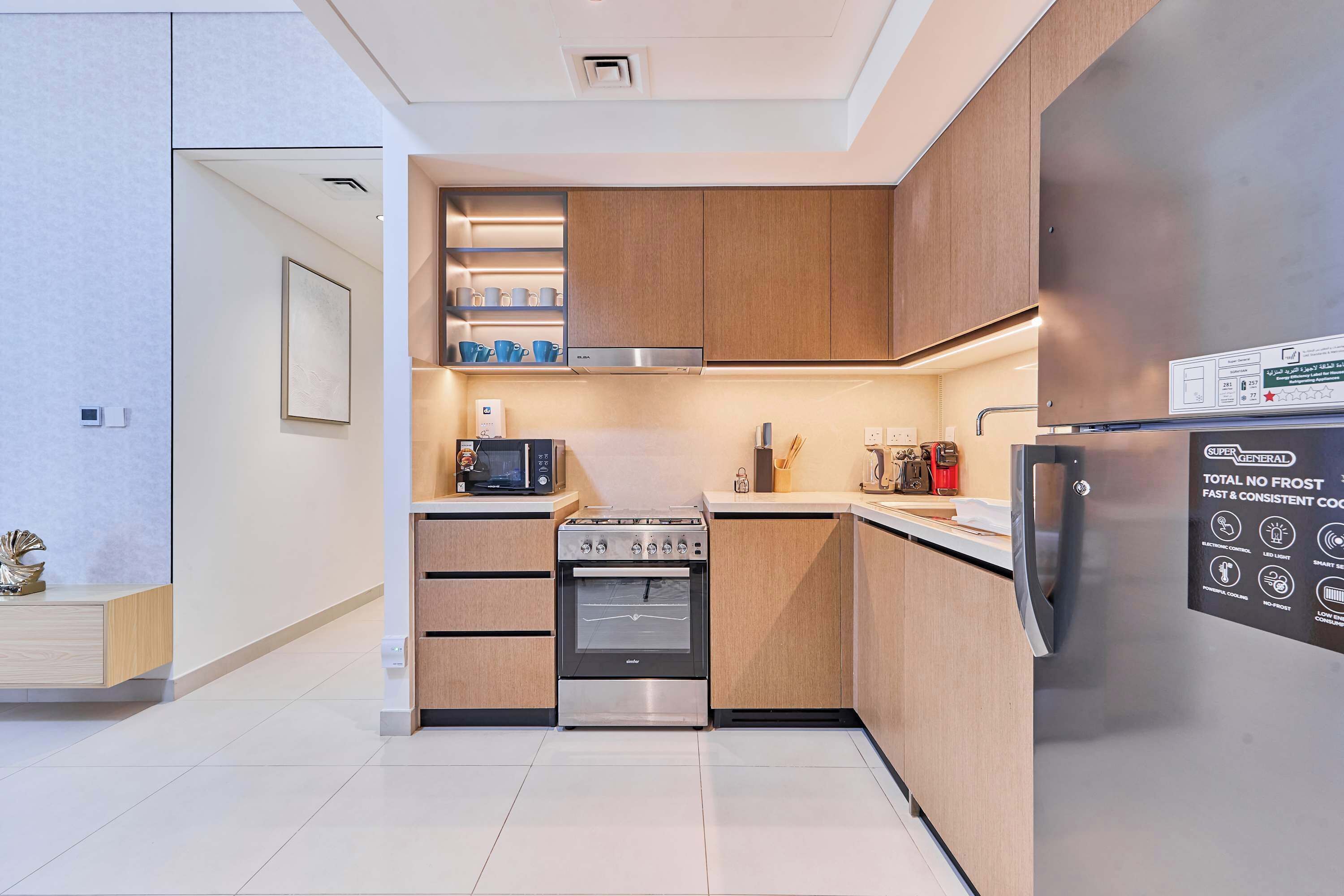 A modern kitchen with wooden cabinets, a stainless steel refrigerator, a microwave, an oven, and a sink.