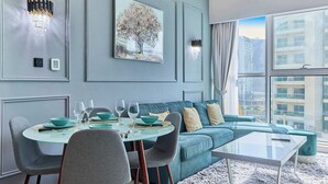 A modern living room with a teal sofa, a glass coffee table, and a dining area with a round table and chairs. - Luxury 1BHK with Stunning Canal View Business Bay (Dubai)