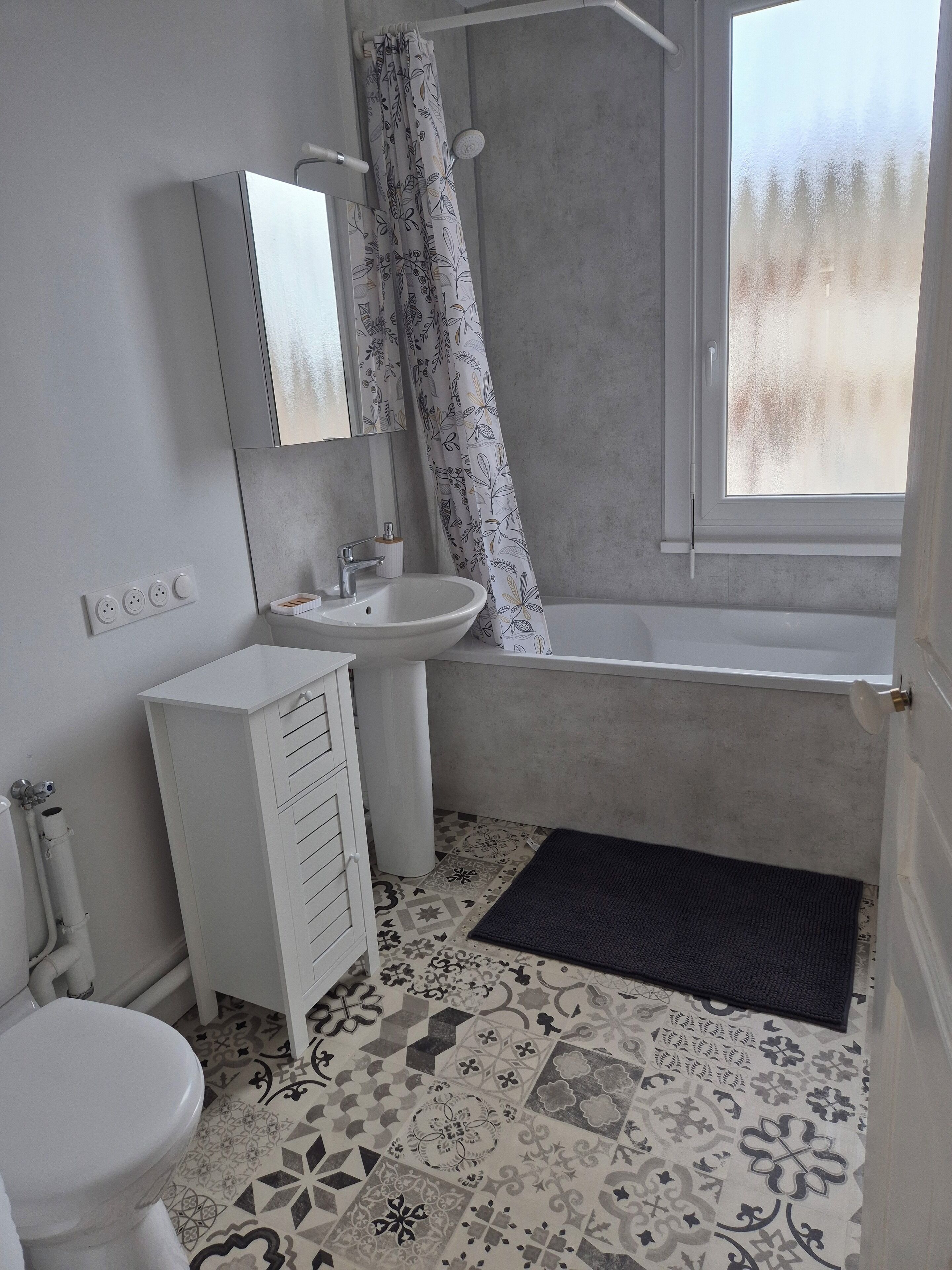 Un bagno con WC, lavabo e vasca. Si vede una finestra con vista sugli alberi. Il pavimento è rivestito di piastrelle decorate.