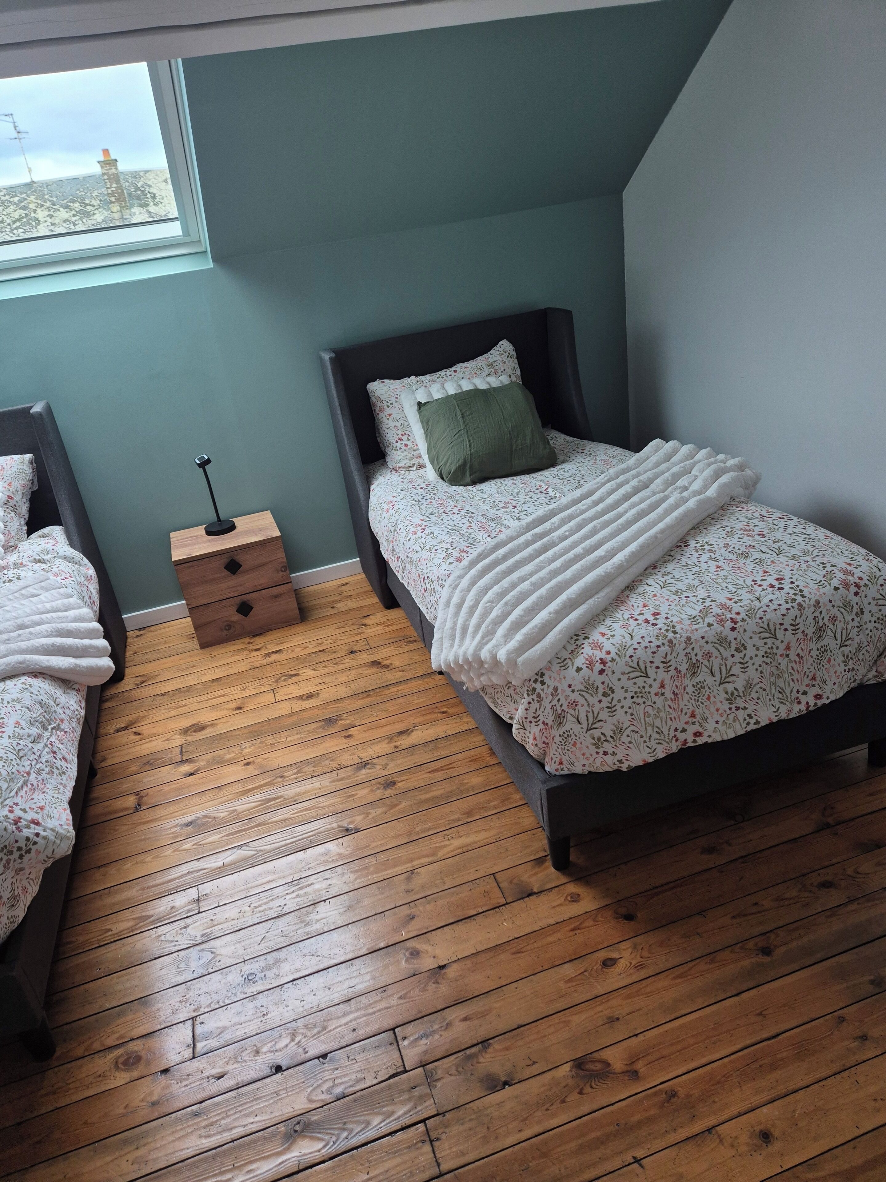 A bedroom with two single beds, a nightstand, a window, and a wooden floor.