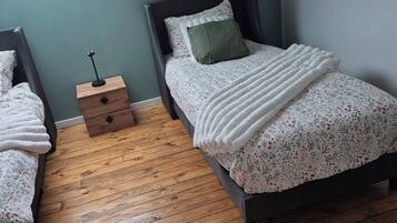 A bedroom with two single beds, a nightstand, a window, and a wooden floor.