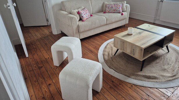 Ein Wohnzimmer mit einem gestreiften Sofa, zwei weißen Poufs, einem Holztisch und einem runden Teppich.