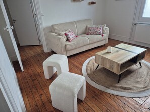 A living room with a striped sofa, two white poufs, a wooden coffee table, and a round rug. - Apartment-cosy-nature tres proche-centre-ville proche-au calme (Cambrai)