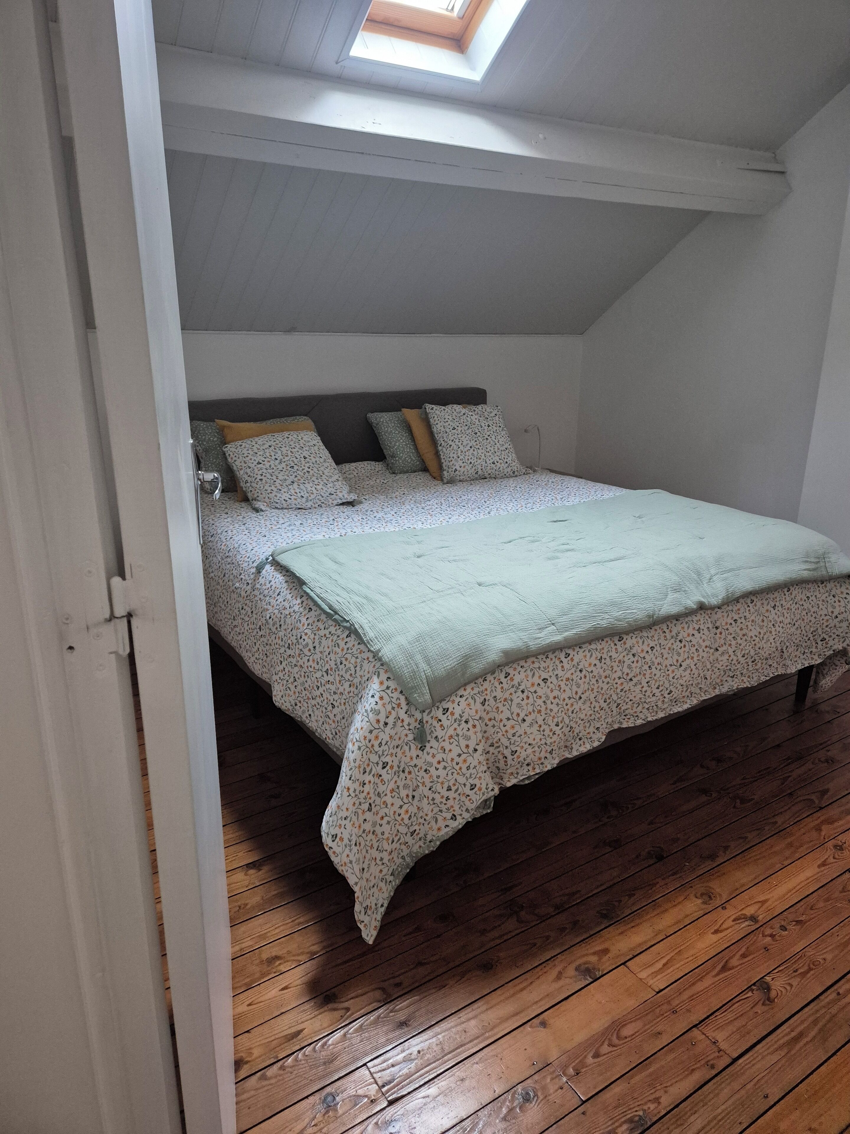 Un dormitorio con techo inclinado, tragaluz, cama con ropa de cama floral y suelo de madera.