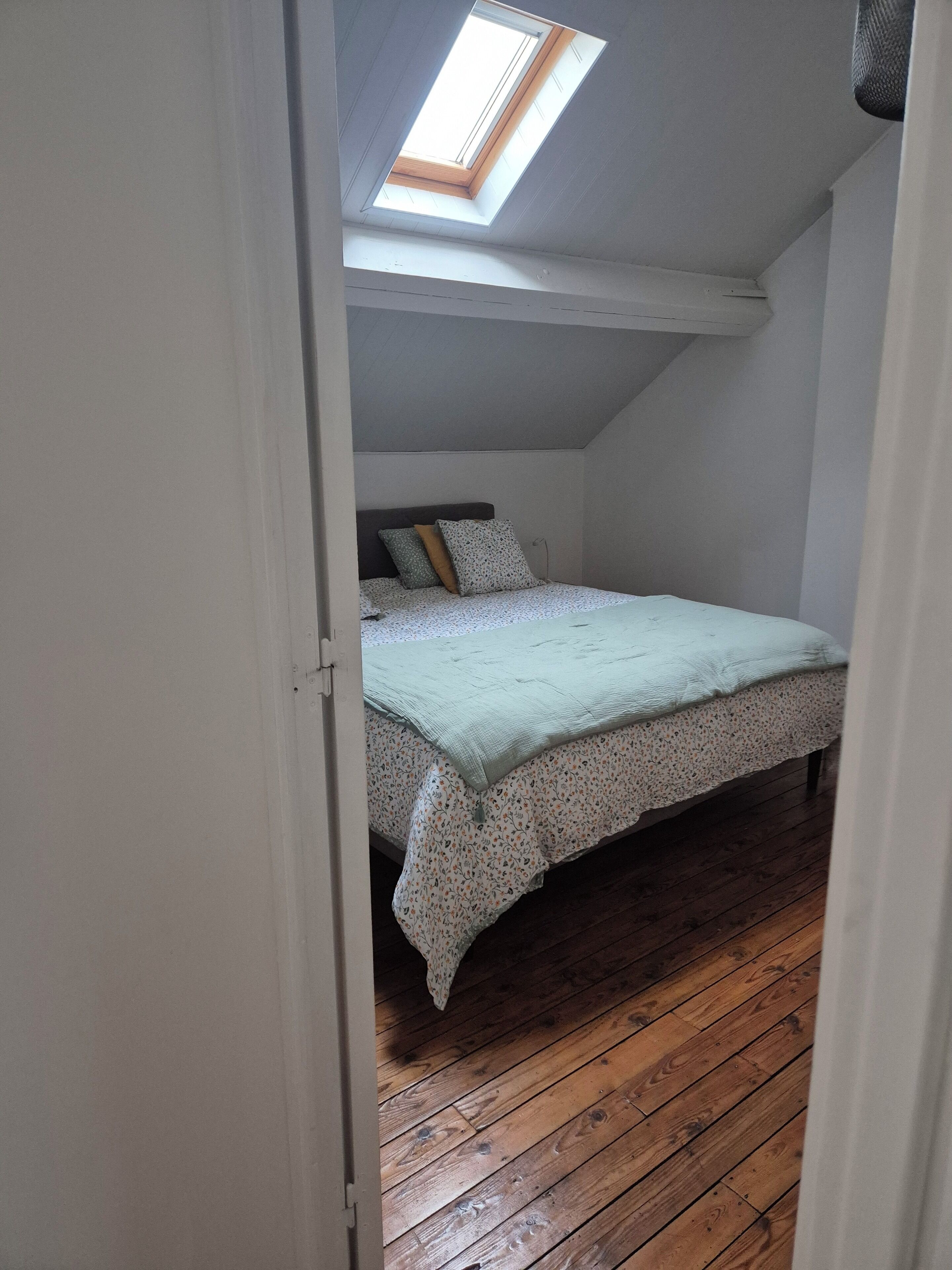 A bedroom with a sloped ceiling, a skylight, a bed with floral bedding, and wooden flooring.