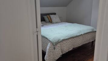 A bedroom with a sloped ceiling, a skylight, a bed with floral bedding, and wooden flooring.