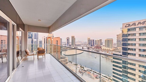 A balcony with a view of a cityscape, including a river and modern buildings. - Cityscape Comforts 2BR (Dubai)