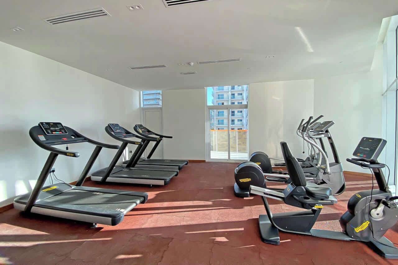Une salle de sport équipée de tapis de course, de vélos elliptiques et de postes d'entraînement avec poids.